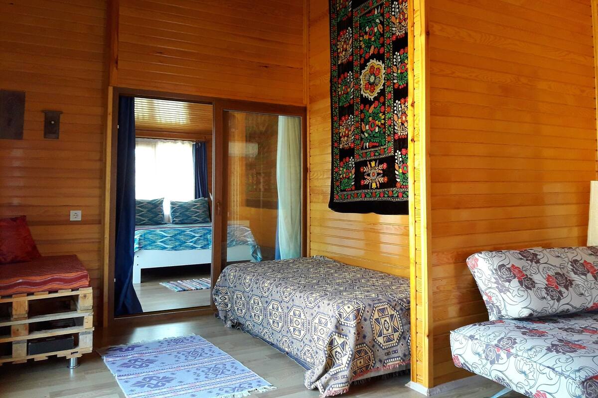 A cozy room with wooden walls, a bed with patterned bedding, a small sofa, and a decorative tapestry.