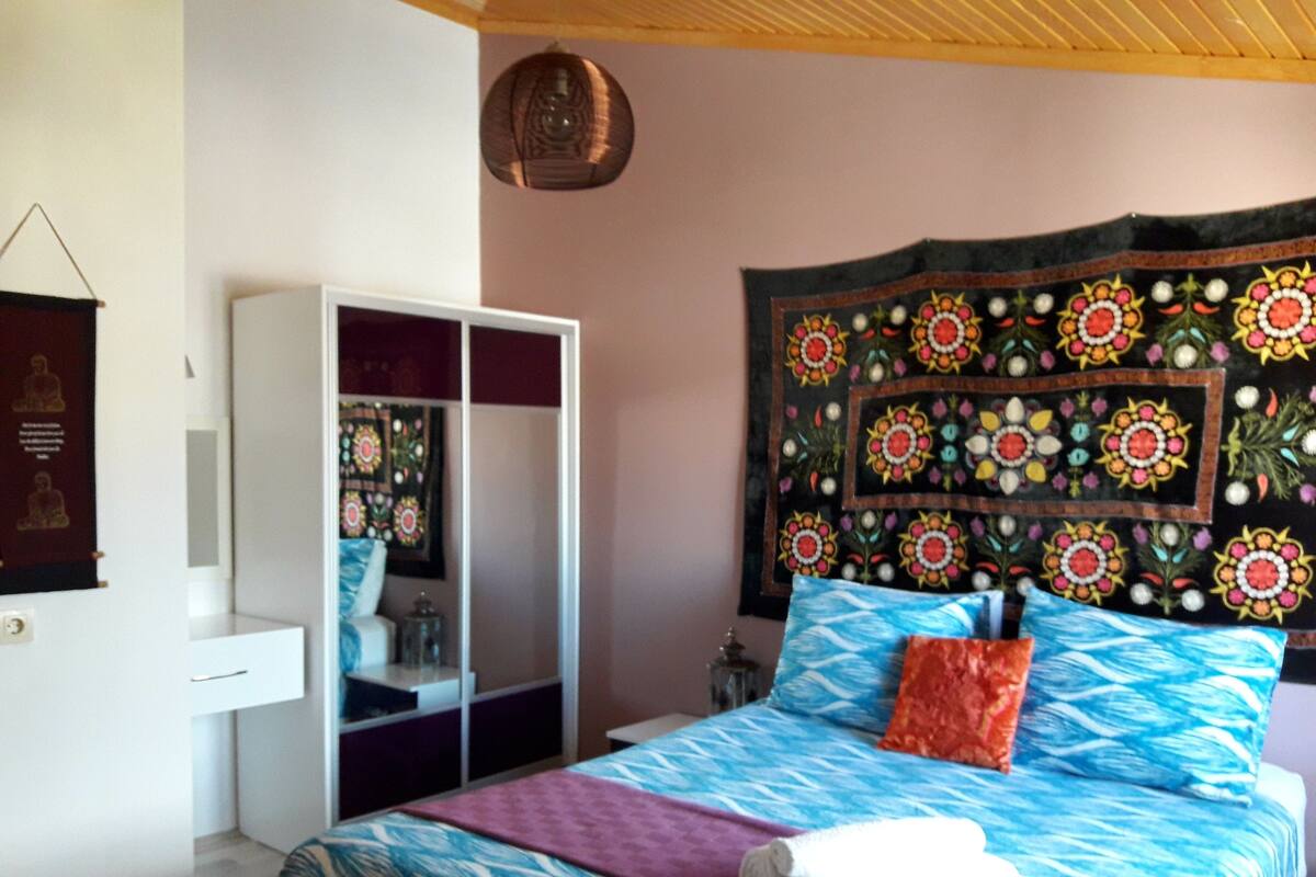 A bedroom with a bed, a wardrobe, a tapestry, and a hanging light fixture.