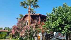 Un edificio in legno con un balcone, immerso nel verde e circondato da fiori rosa.