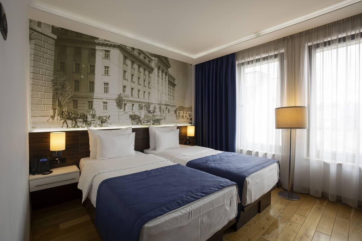 A hotel room with two beds, a large mural on the wall, a desk with a lamp, and a floor lamp.