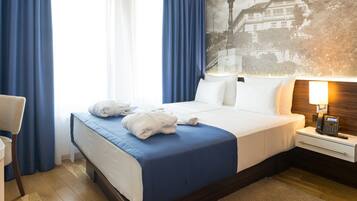 Quarto de hotel com cama bem arrumada, mesa de cabeceira com abajur e uma janela grande com cortinas.