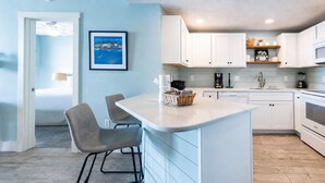 Una cocina moderna con armarios blancos, una isla central y un comedor con dos sillas.
