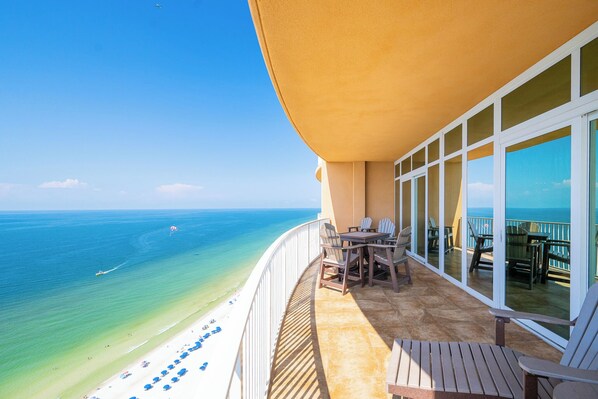 A balcony with a view of the ocean, a table with chairs, and a sunshade.