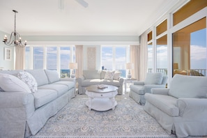 A spacious living room with a large window, a chandelier, and a patterned rug.