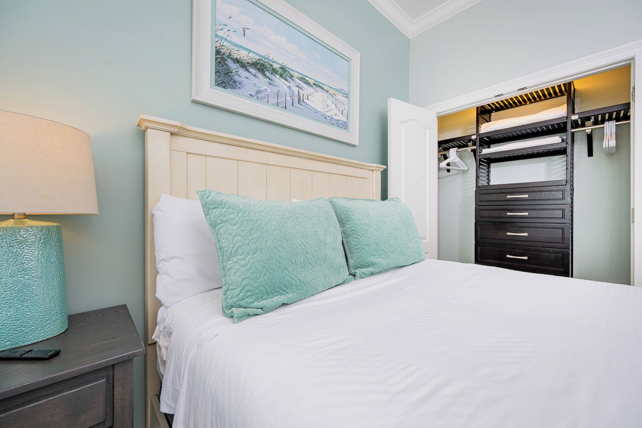 A neatly made bed with two pillows, a bedside lamp, and a painting above it.