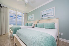 Une chambre avec deux lits, une vue sur la plage et un ventilateur de plafond.