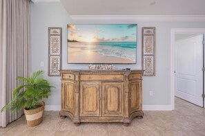 Ein Holzschrank mit dekorativen Paneelen, ein großes gerahmtes Bild mit einer Strandansicht und ein Topfpflanze.
