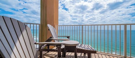 A balcony with two Adirondack chairs and a small round table, overlooking a clear blue ocean.