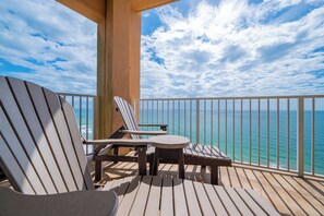 Un balcon agrémenté de deux fauteuils Adirondack et d’une petite table ronde, offrant une vue imprenable sur un océan d’un bleu profond.