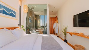 A modern hotel room with a large bed, a television, a wooden shelf with decorative items, and a view of the bathroom and outside. - Floral Holiday Guesthouse (Dali)
