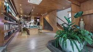 A modern interior with wooden floors, a central staircase, a reception desk, and a large potted plant. - Floral Holiday Guesthouse (Dali)
