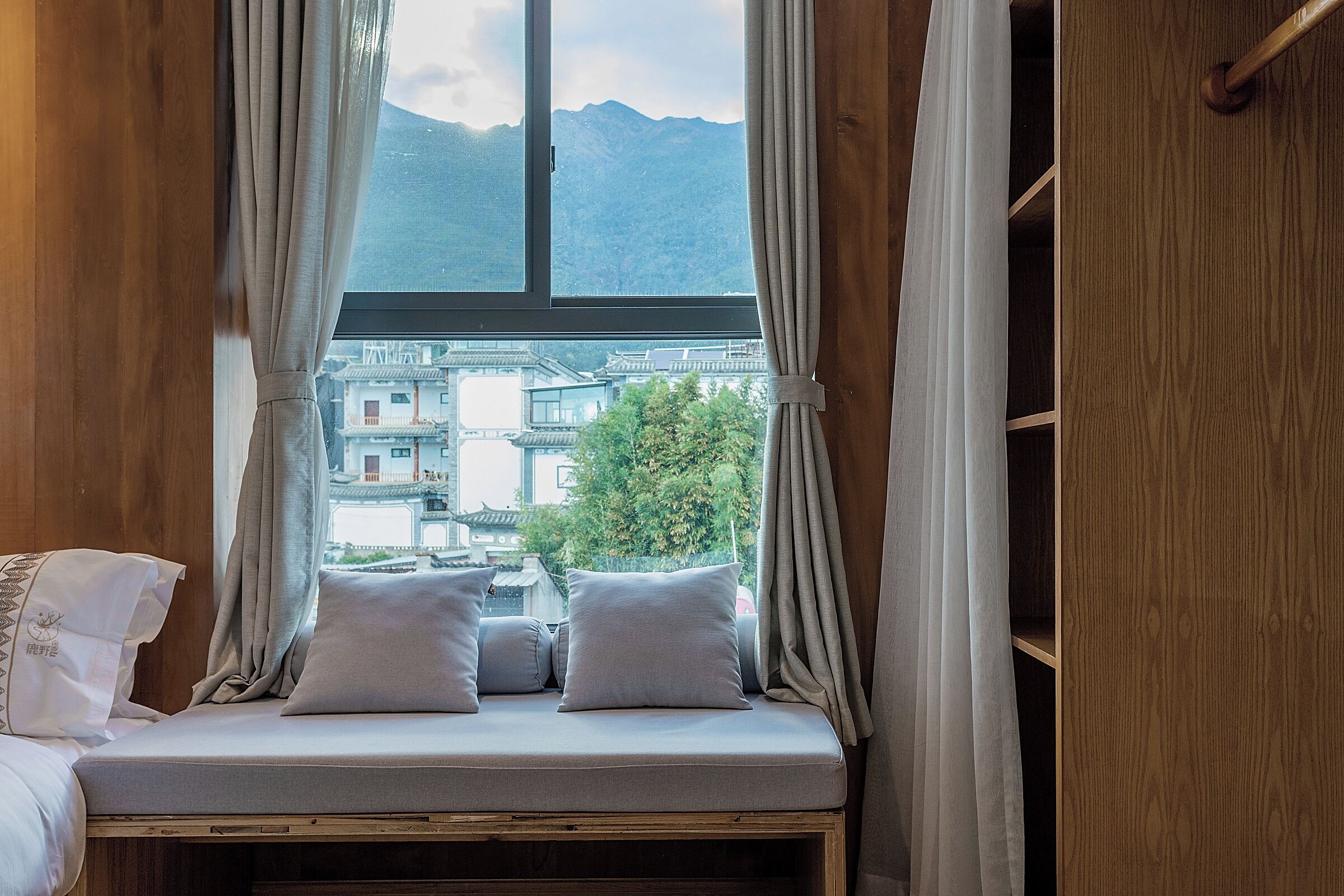 A bed with a view of mountains and traditional buildings through a window.