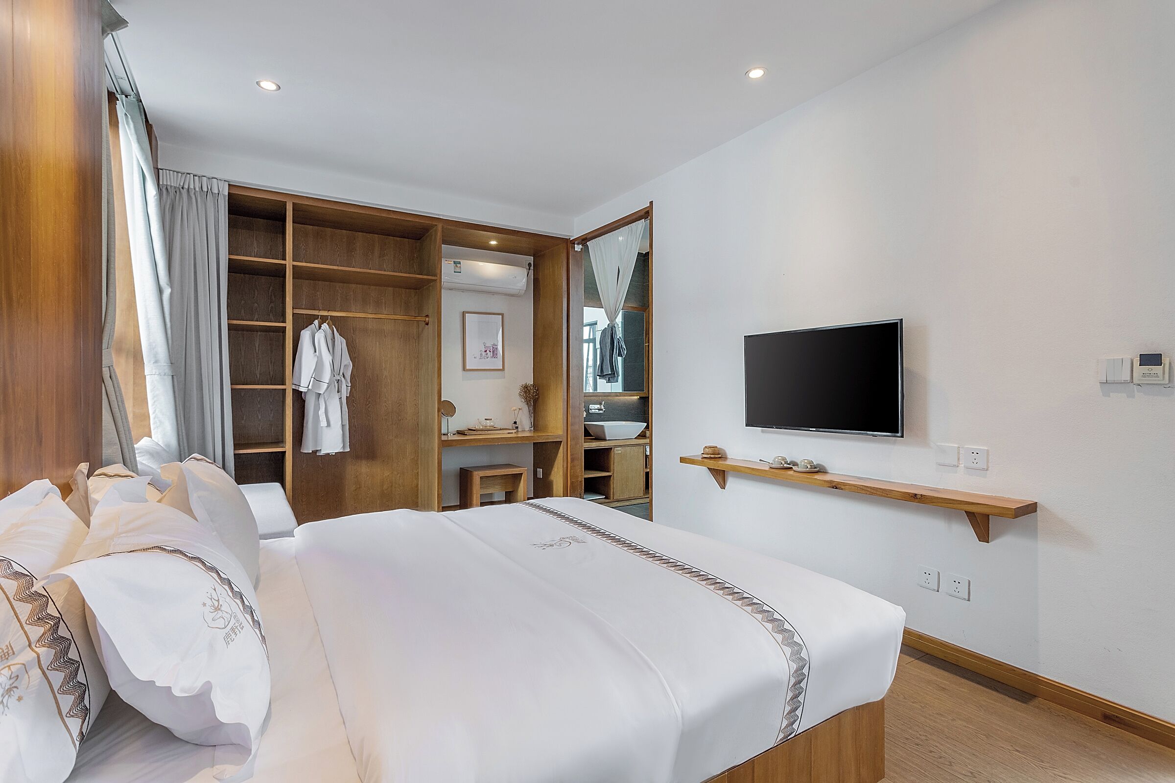 A hotel room with a bed, a TV, a wooden wardrobe, and a bathroom visible through an open door.