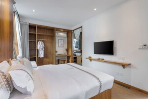 Habitación de hotel con cama, televisor, armario de madera y baño visible a través de una puerta abierta.
