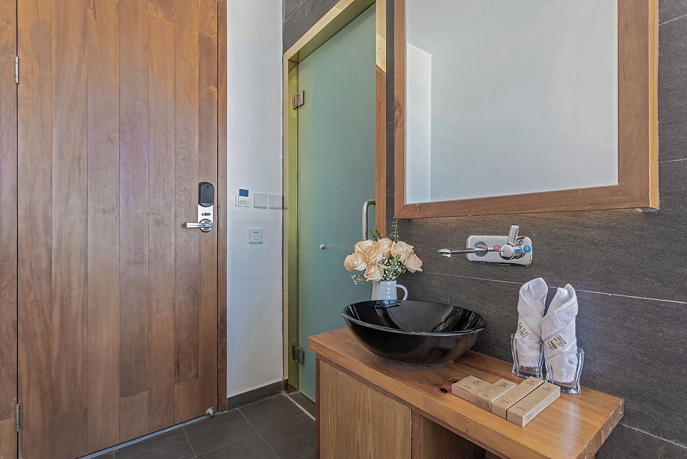 A bathroom with a wooden vanity, a black bowl sink, a mirror, a green door, and a towel rack with towels.