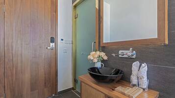 A bathroom with a wooden vanity, a black bowl sink, a mirror, a green door, and a towel rack with towels.