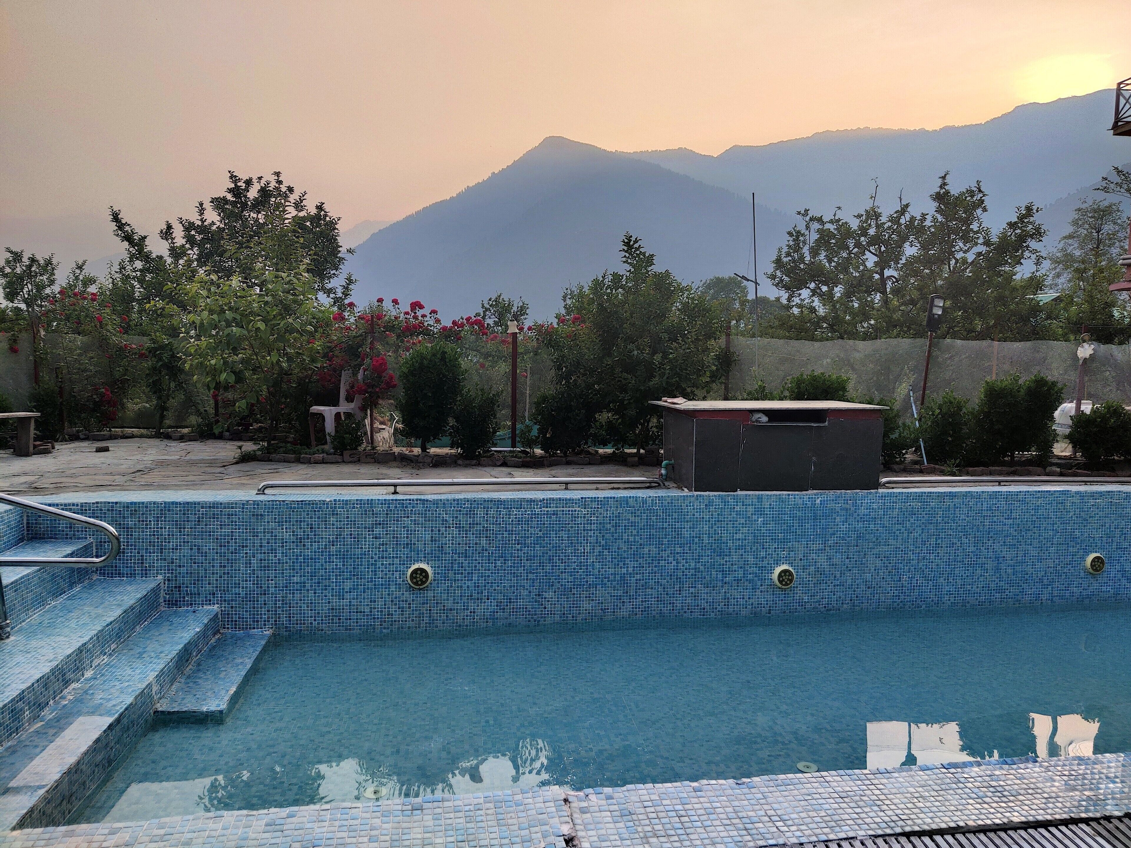 A swimming pool with steps leading into it, surrounded by trees and a view of mountains.
