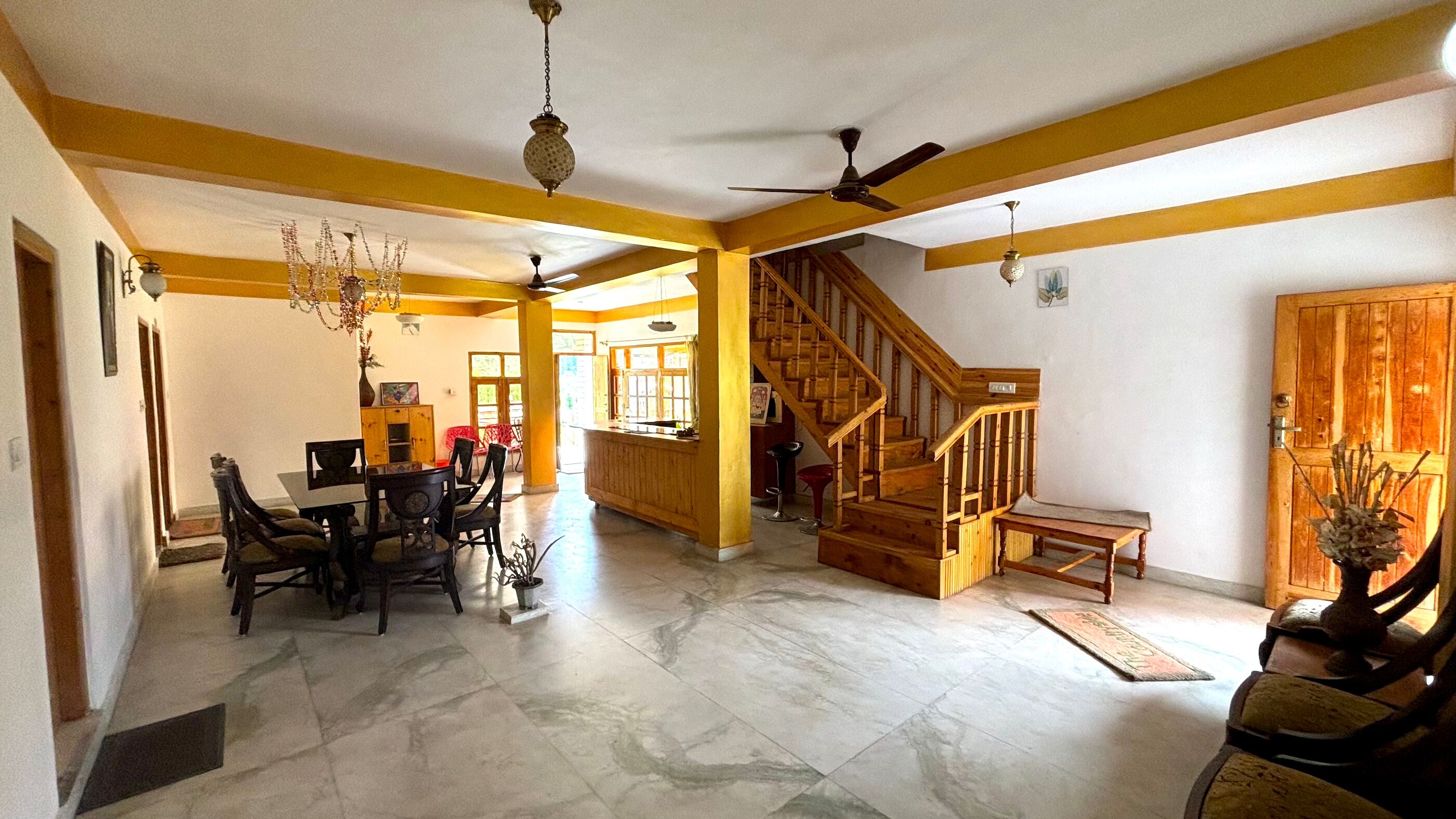 A spacious living area with a dining table, chairs, a staircase, and a chandelier.