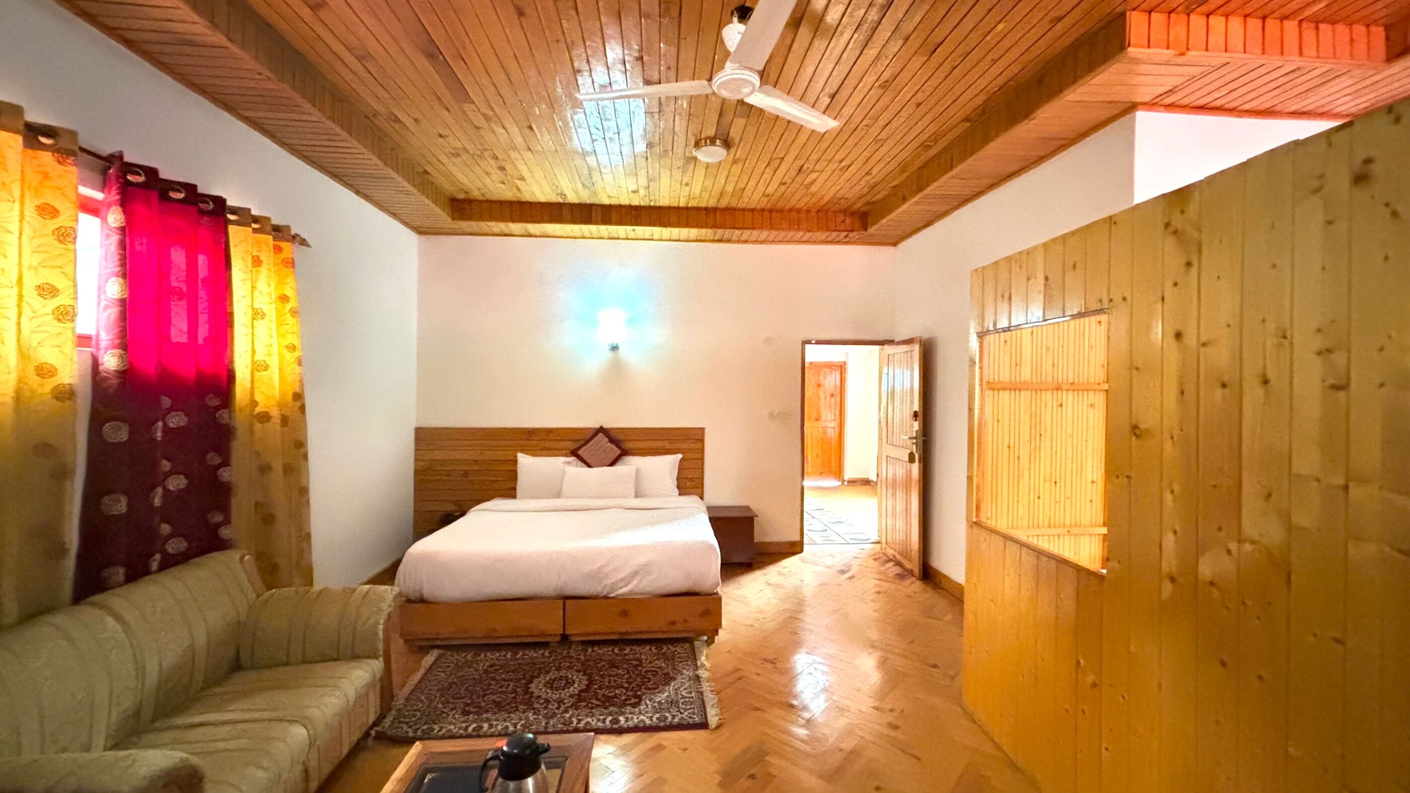 Un dormitorio con techo de madera, una cama con ropa de cama blanca, un armario de madera y piso de madera.