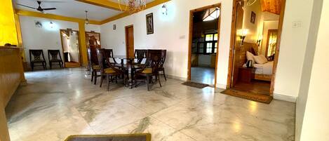 A spacious dining area with a marble floor, wooden chairs, and a chandelier. There are wooden doors leading to other rooms.