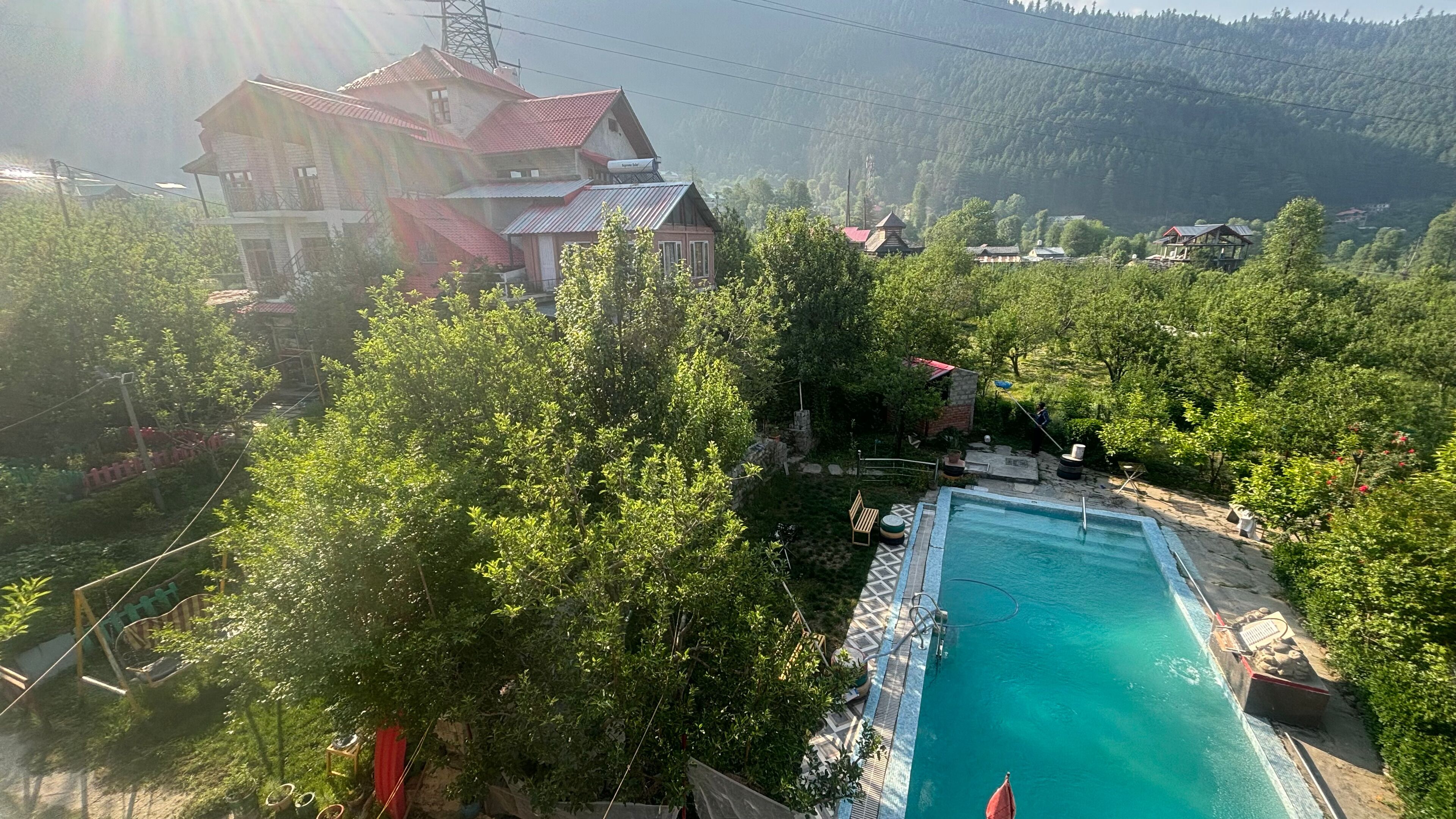 Une piscine entourée d’une végétation luxuriante et un grand bâtiment doté d’un toit rouge.