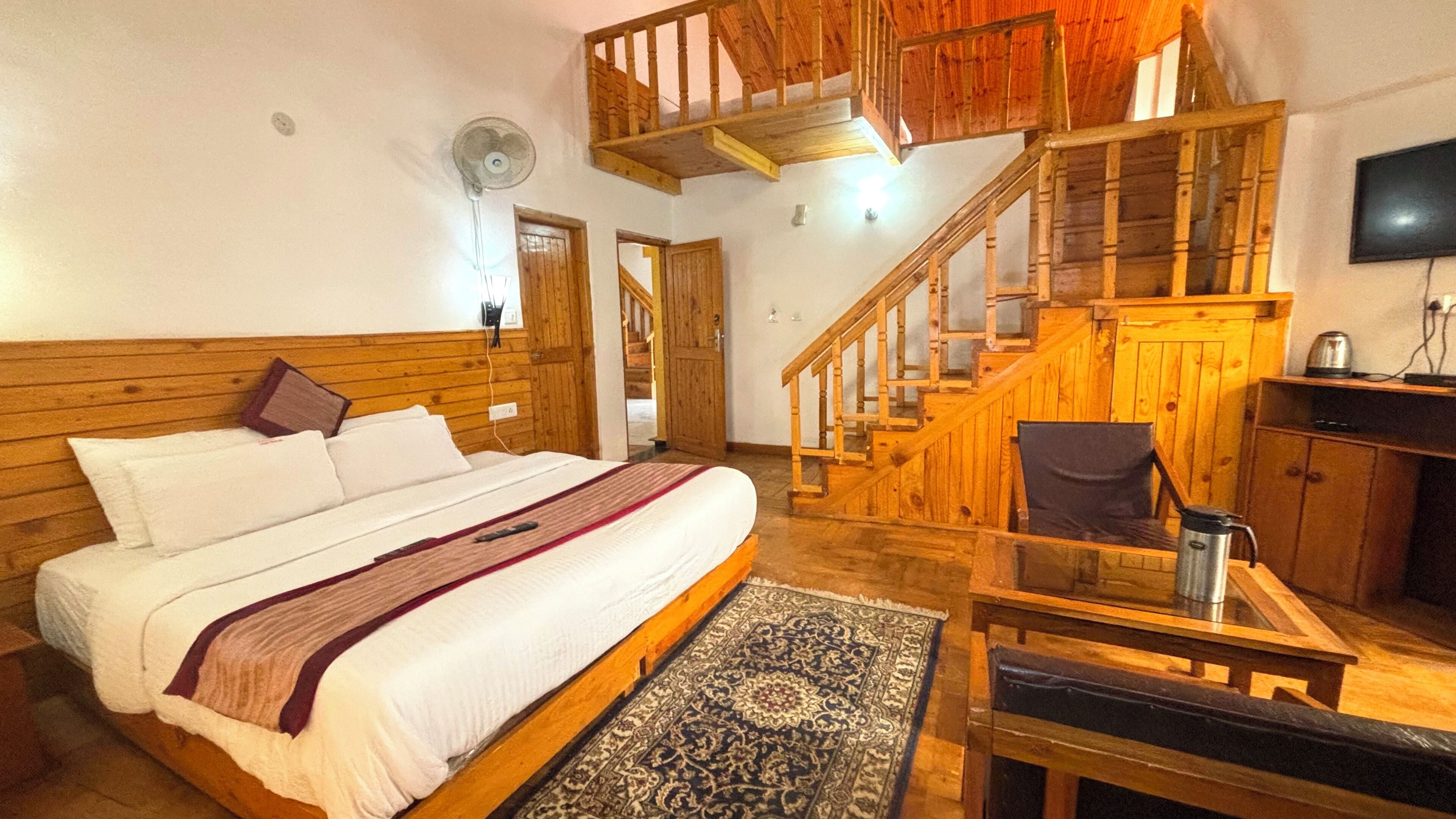 A bedroom with a wooden bed, a small table, a chair, a rug, and a staircase.