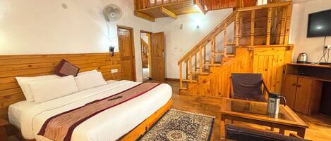 A bedroom with a wooden bed, a small table, a chair, a rug, and a staircase.