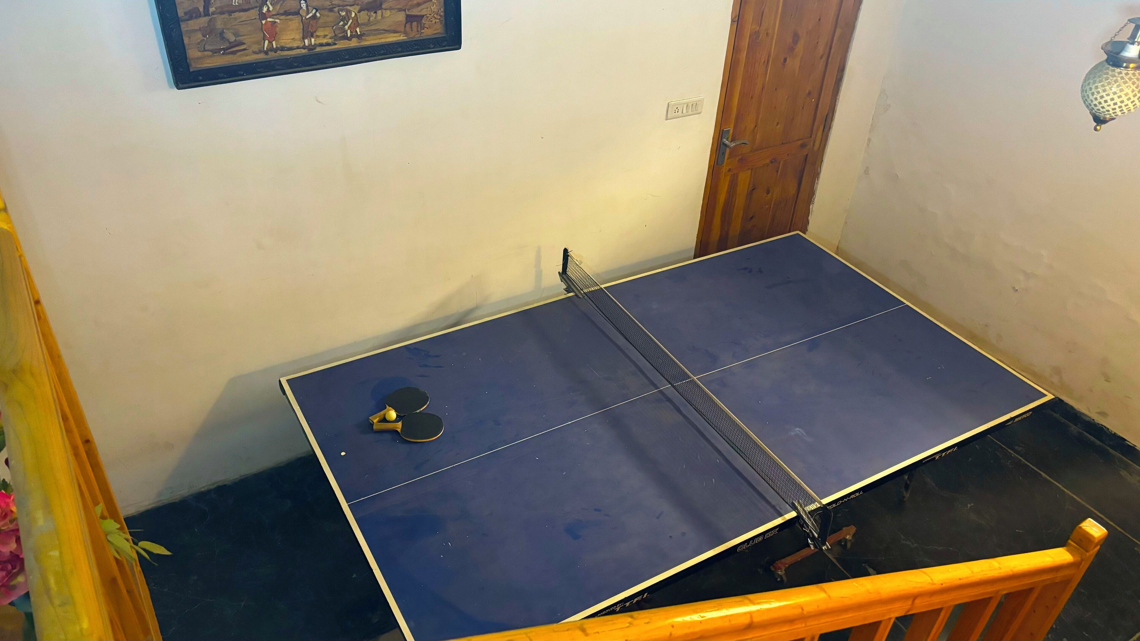 Ein Tischtennis-Tisch mit Netz in einem Raum, der eine Holztür und eine Wandleuchte hat.