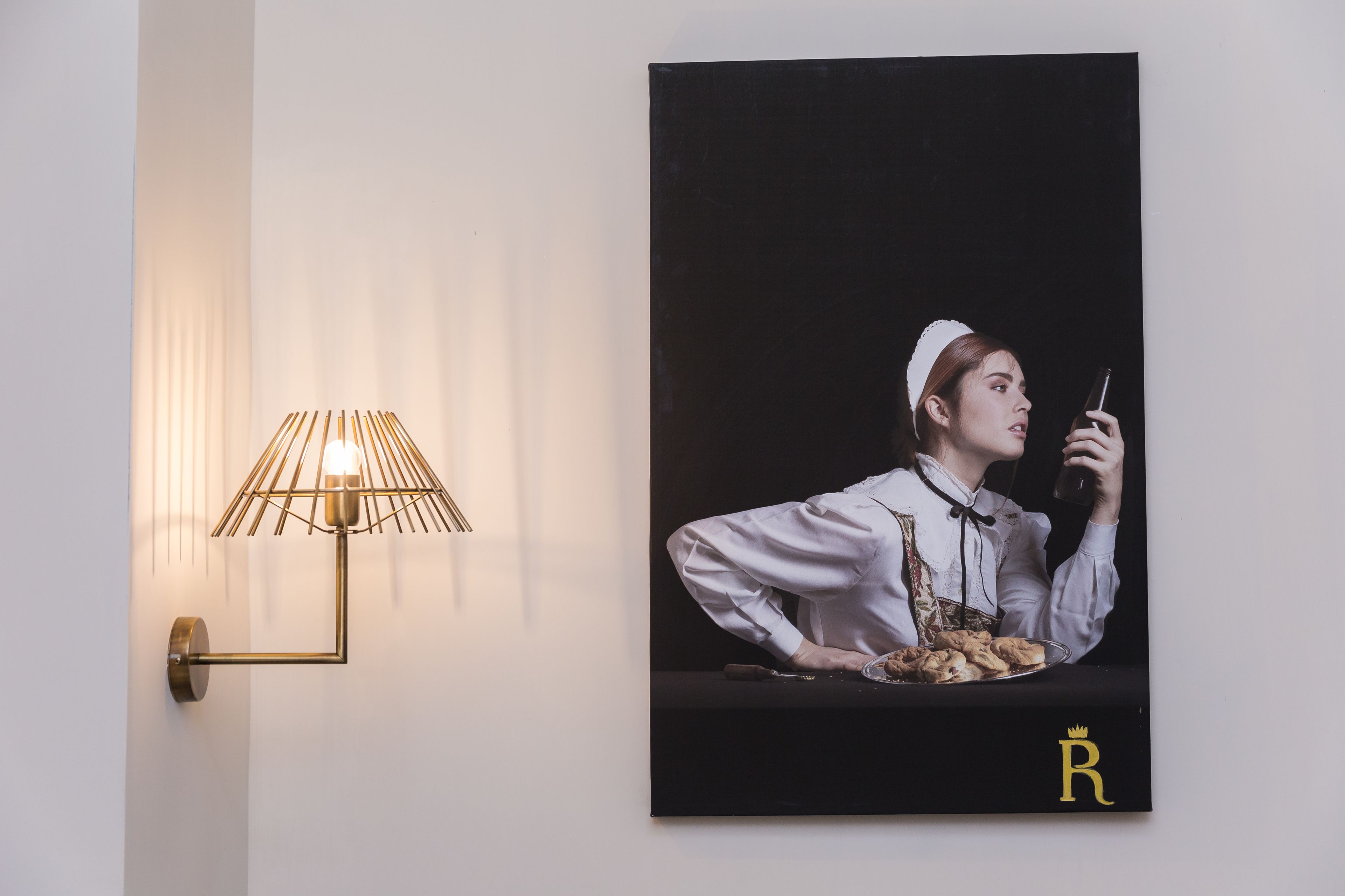 A wall-mounted lamp with a geometric design and a framed portrait of a person holding a glass.
