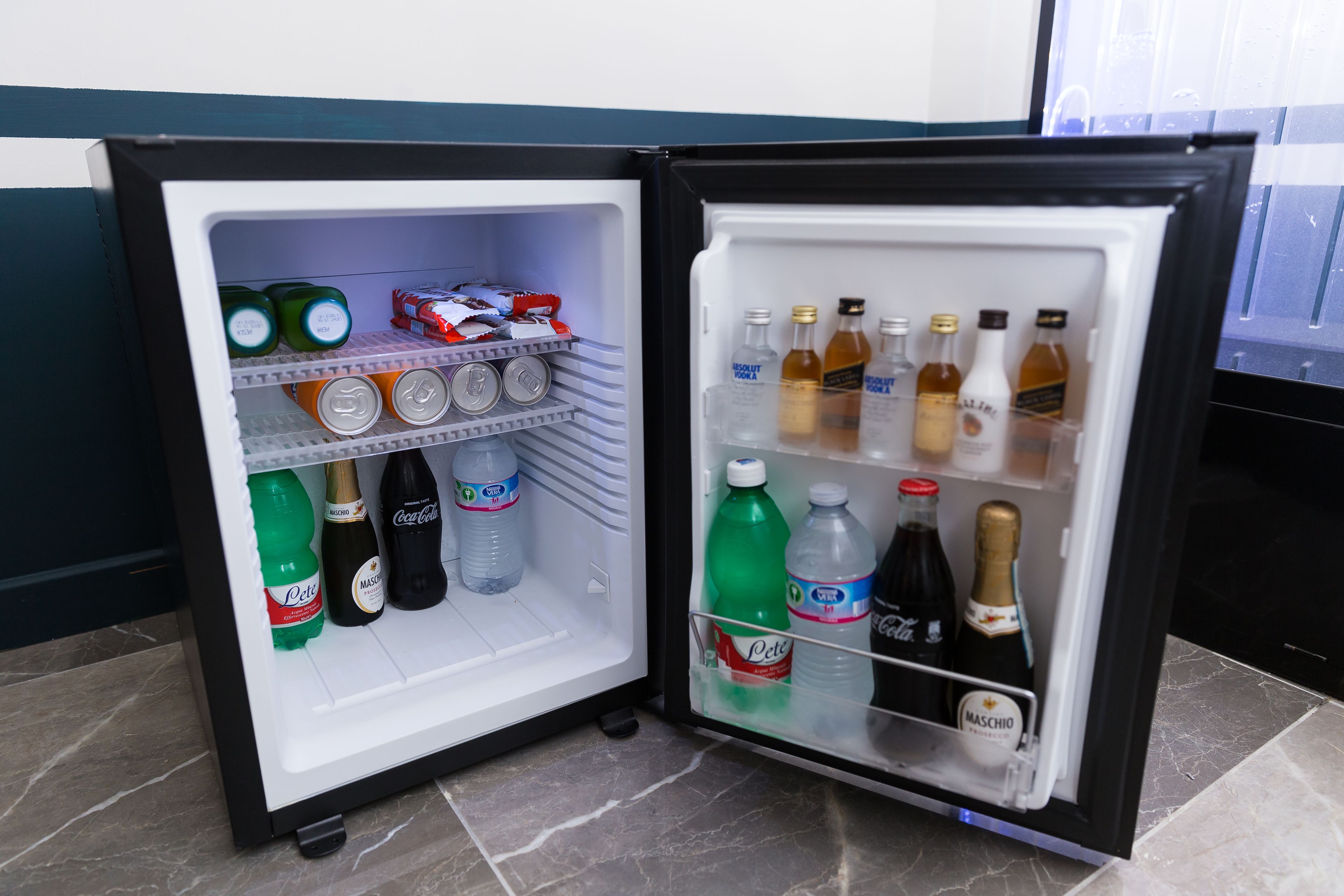 Un mini-réfrigérateur doté d’étagères contenant diverses boissons, notamment des sodas, de l’eau en bouteille et des boissons alcoolisées.
