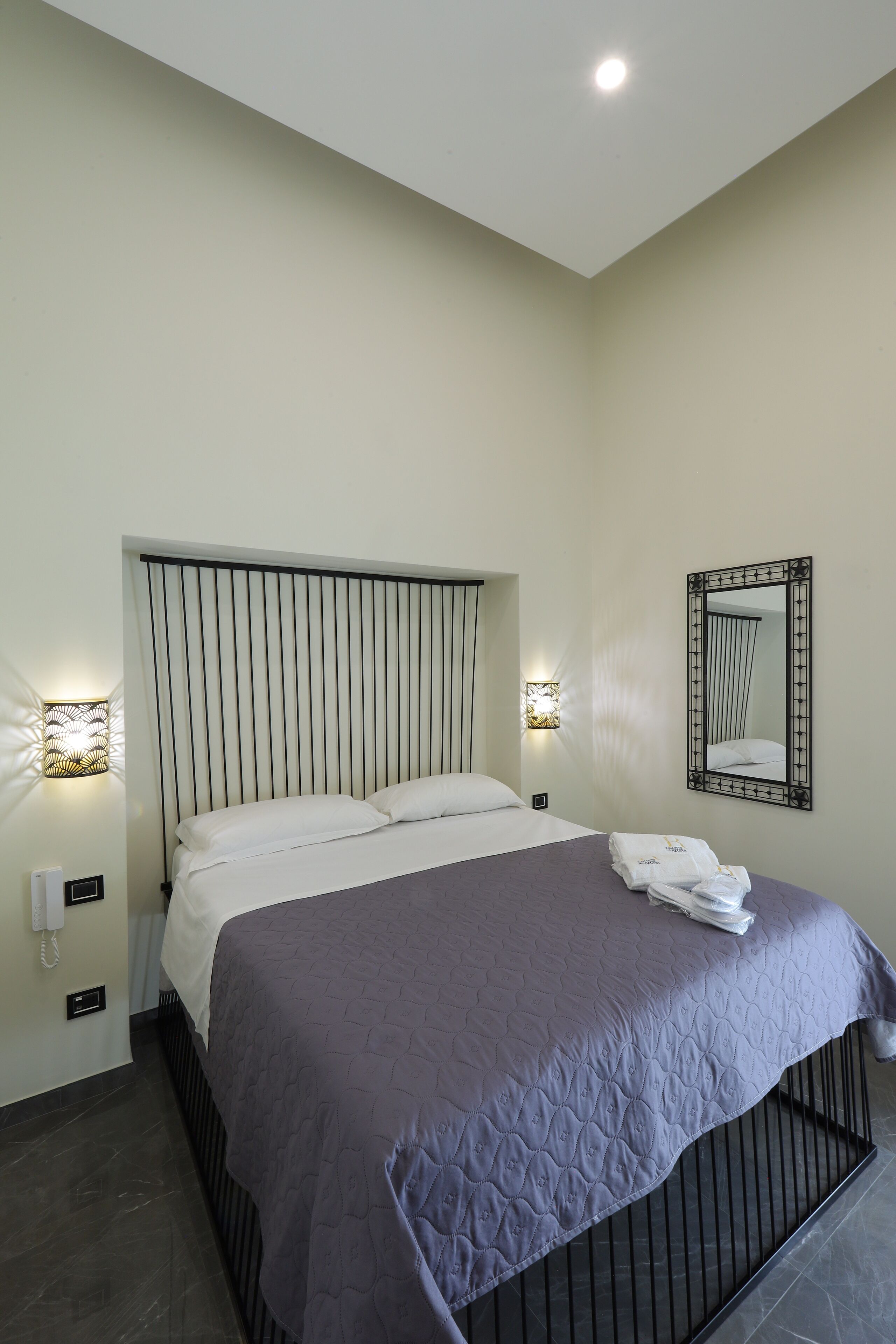 Une chambre d’hôtel moderne avec un grand lit, une tête de lit ornée de lignes verticales, un miroir fixé au mur et deux lampes de chevet.