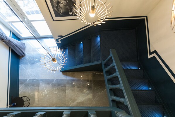 Una escalera moderna con barandilla de metal, tragaluz y una lámpara de pared de diseño único.