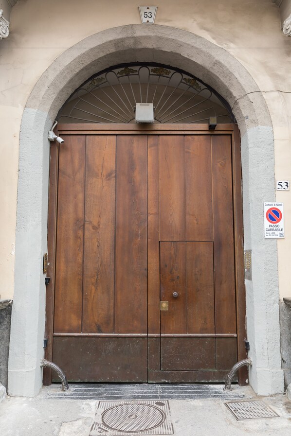 Una puerta de madera grande con una reja metálica, el número "53" arriba y un letrero de no estacionamiento a la derecha.