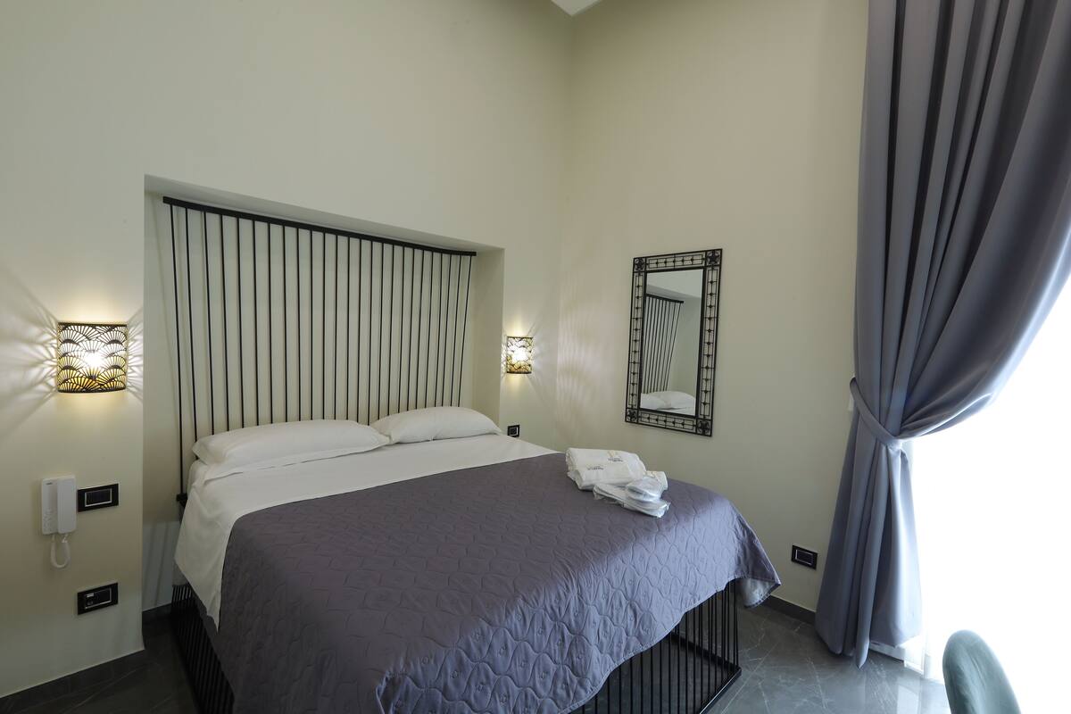 Une chambre d’hôtel avec un lit, des lampes de chevet, un miroir et un rideau.