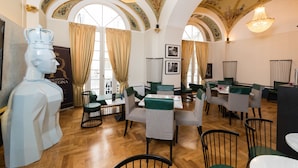 Un comedor con piso de madera, sillas tapizadas en verde y gris, y una araña.