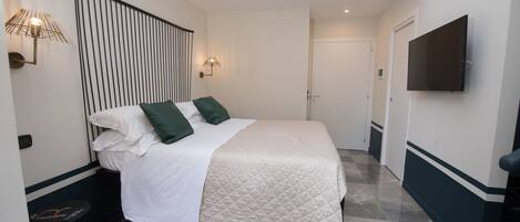 A neatly arranged bedroom with a bed, bedside lamps, a flat-screen TV, and a door leading to another room.