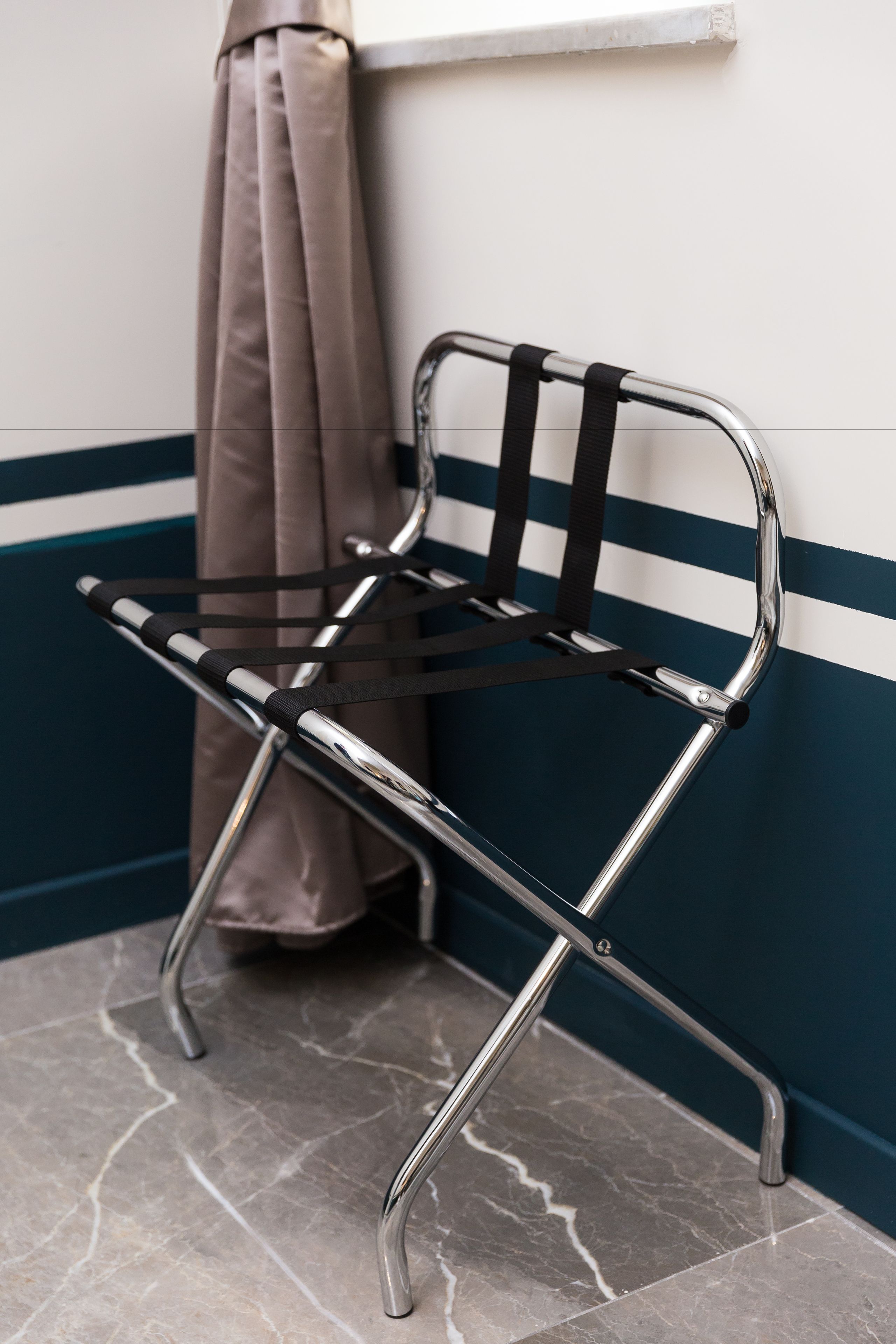 Una silla de estructura metálica con correas negras, ubicada frente a una pared con una franja azul.
