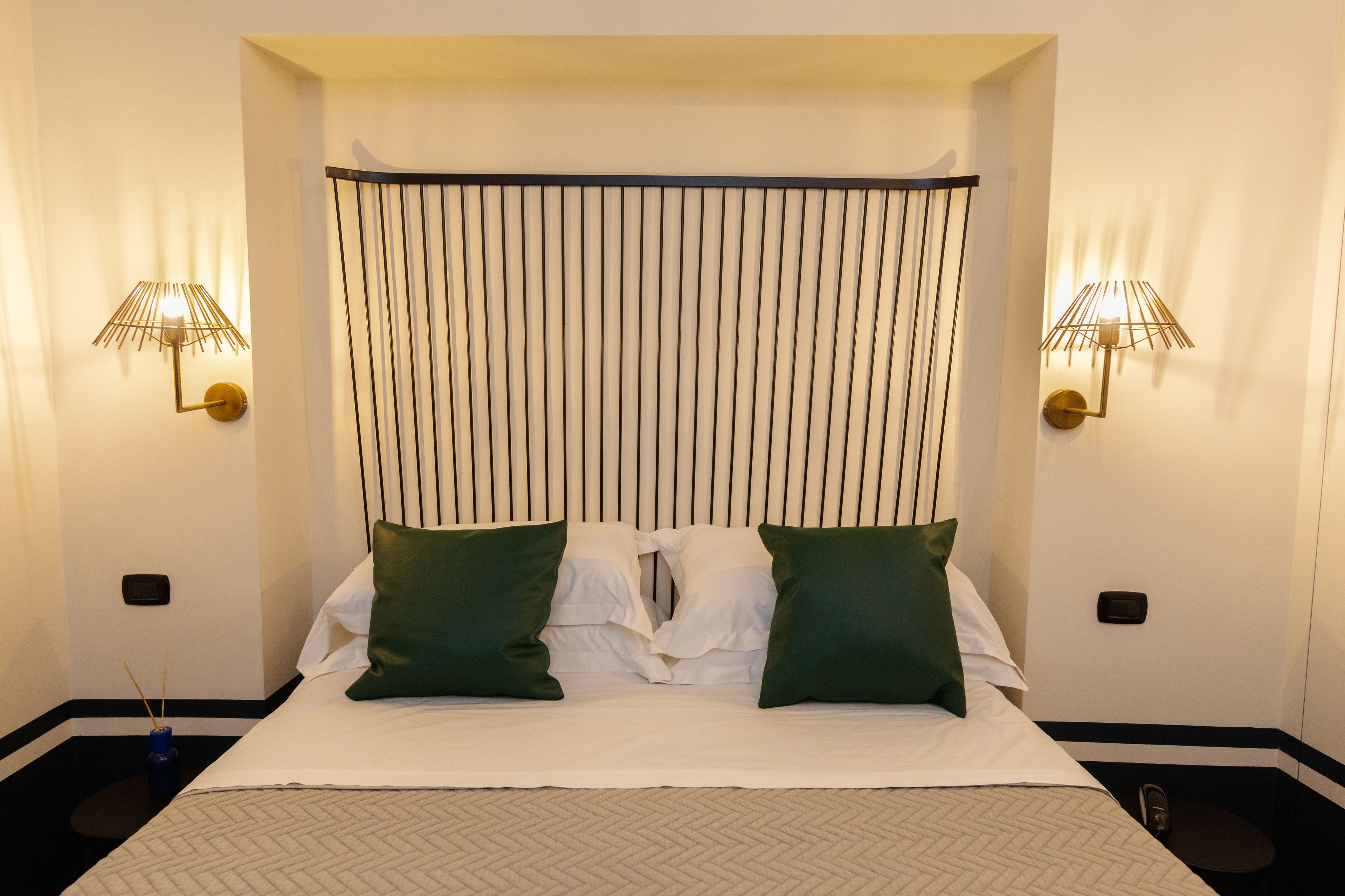 A hotel room with a bed, two green pillows, a white comforter, and two wall-mounted lamps.