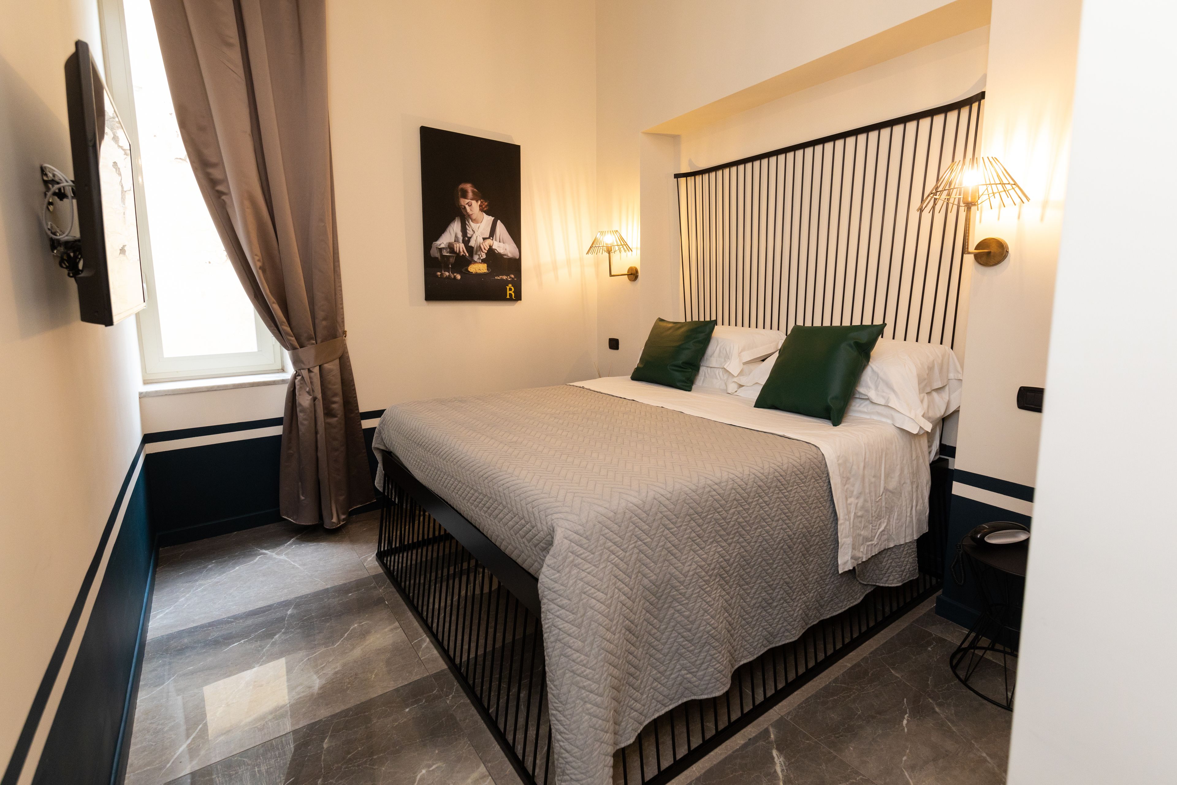 Une chambre bien rangée, avec un lit, une table de chevet, une lampe fixée au mur et une fenêtre avec des rideaux.