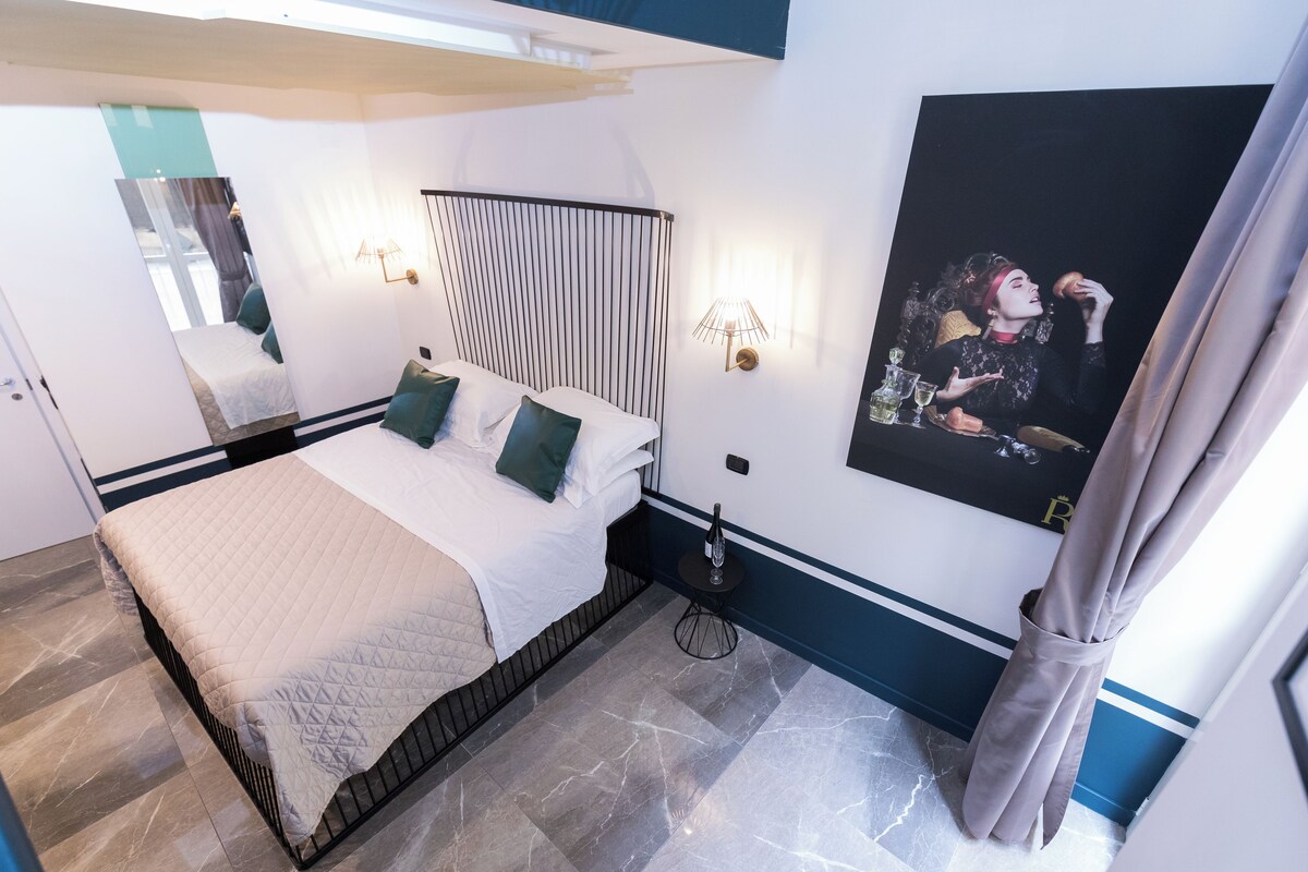 Habitación de hotel moderna con una cama grande, una mesita de noche, una lámpara de pared, un cuadro y una cortina.