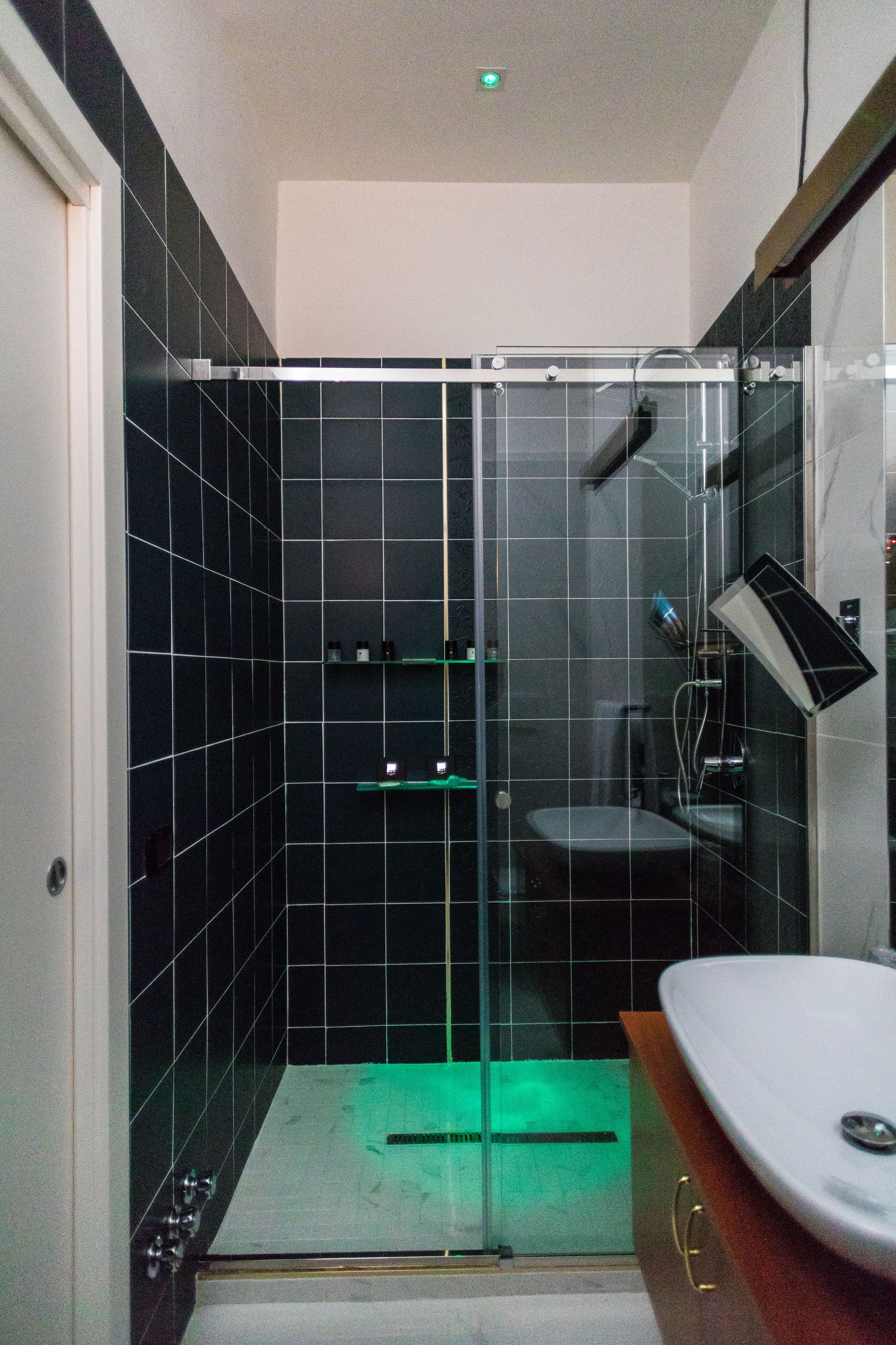 A modern bathroom with a glass-enclosed shower, a white sink, and a tiled wall.