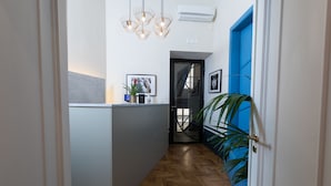 Un pasillo con una mesa de recepción, una puerta azul y una escalera que sube a un nivel superior.