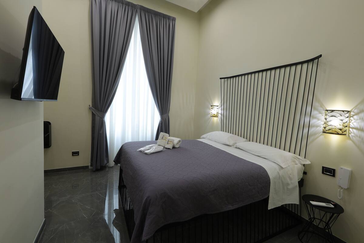 Une chambre d’hôtel moderne dotée d’un grand lit, d’un téléviseur à écran plat, d’une table de chevet avec un téléphone et d’un luminaire fixé au mur.