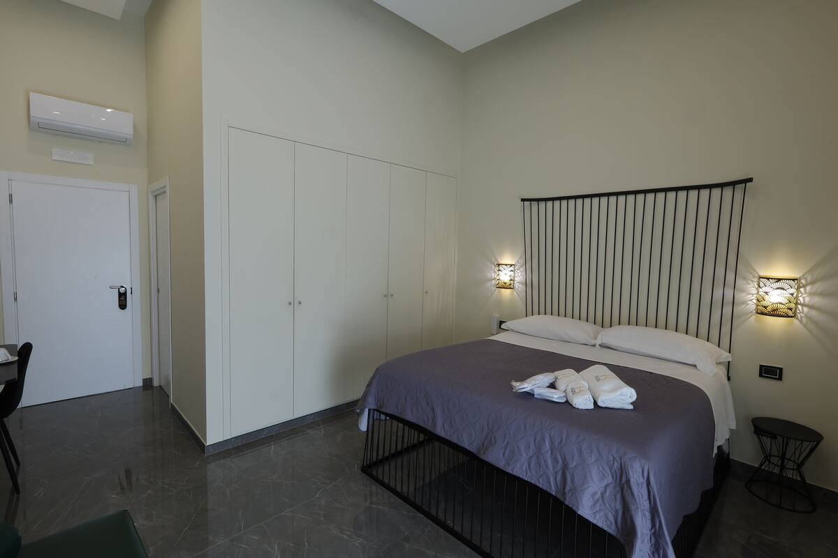 Une chambre d’hôtel moderne avec un lit, un bureau et une chaise. On y trouve également une armoire, un luminaire fixé au mur et une petite table.