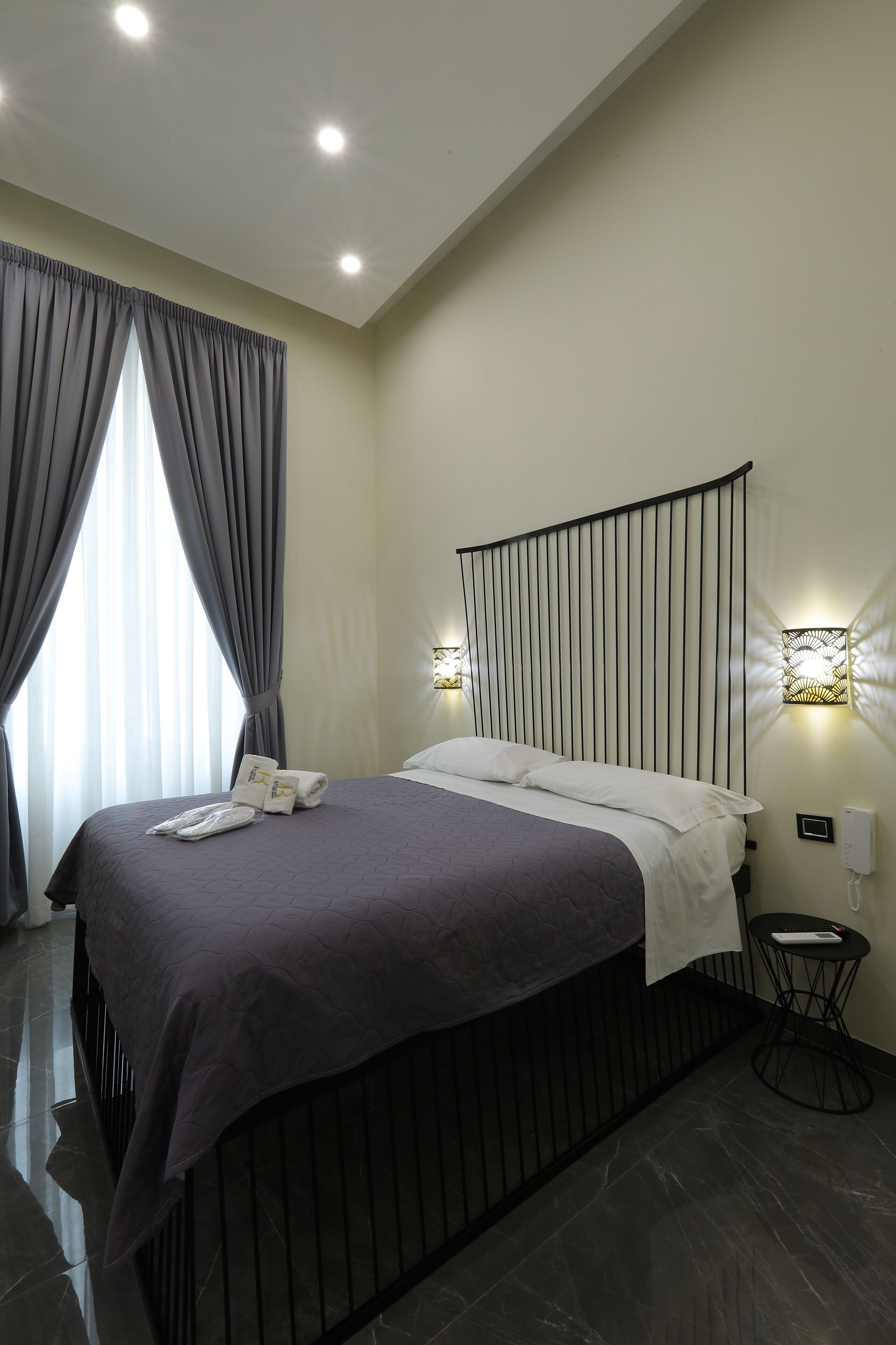 A modern hotel room with a large bed, dark wood headboard, and two wall-mounted lights.