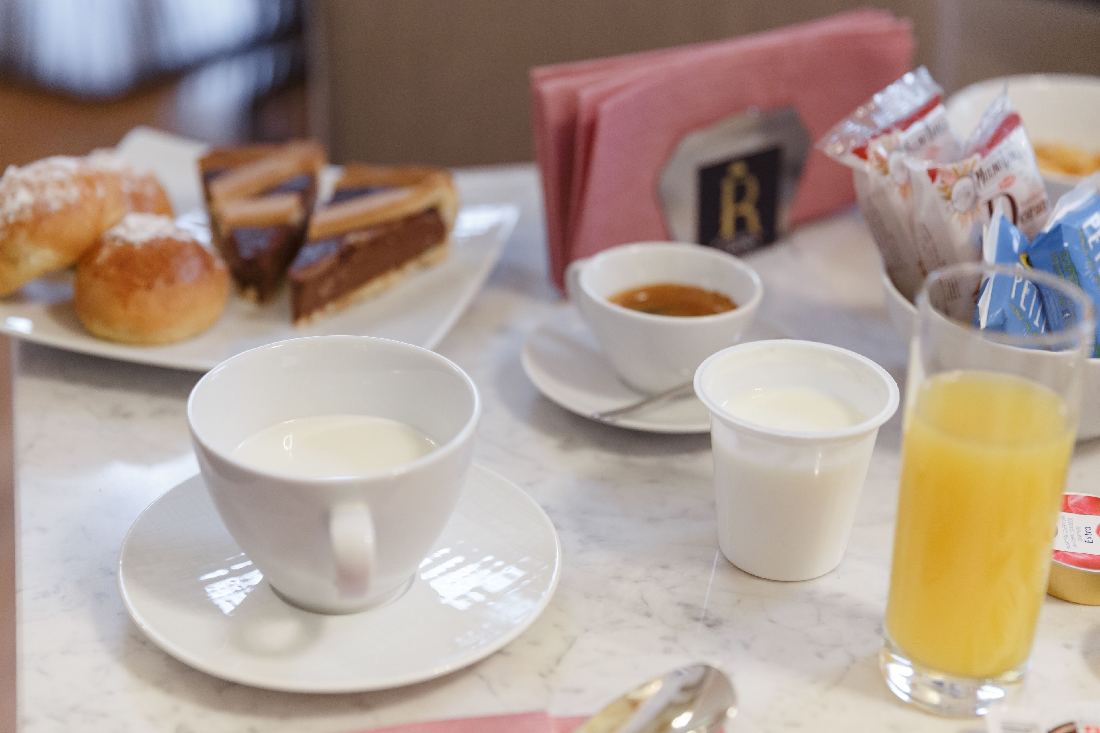 A breakfast setting with pastries, coffee, and juice on a marble table.