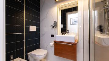Une salle de bain moderne avec des toilettes blanches, un bidet, un meuble-lavabo avec un miroir et un espace douche.