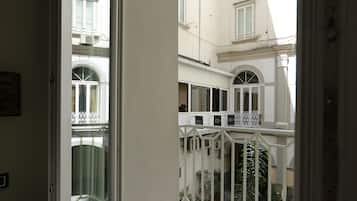 Une vue depuis un balcon, avec la lettre « R » inscrite sur le sol, une balustrade blanche et, en arrière-plan, un immeuble doté de nombreuses fenêtres et de plusieurs balcons.