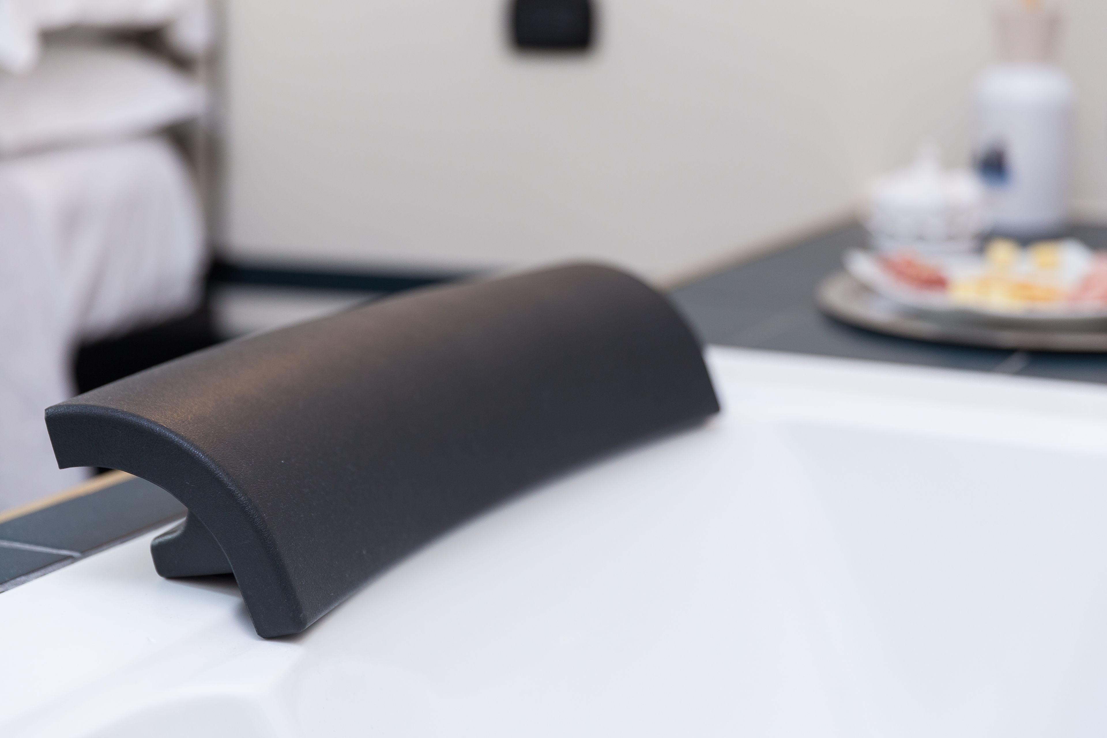 Une pièce moderne et minimaliste, avec un objet noir, élégant et aux lignes courbes, posé sur une surface blanche. Il pourrait s’agir d’un meuble ou d’un appareil.