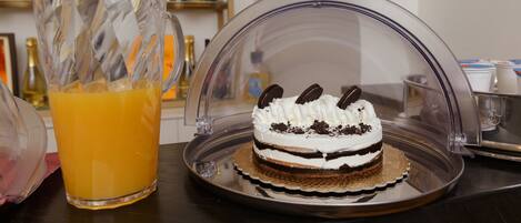 A dessert with a clear dome cover, a pitcher of orange juice, and bottles in the background.